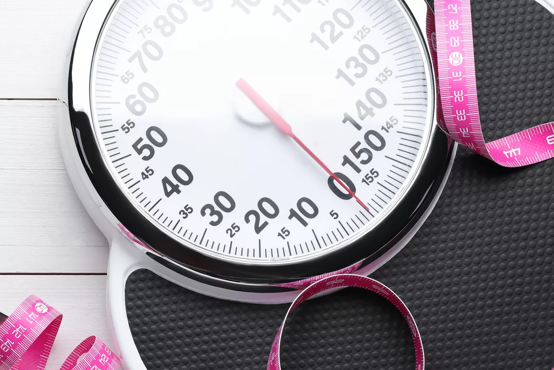Bathroom scale, measuring tape and space for text on white wooden floor, top view. Weight loss concept
