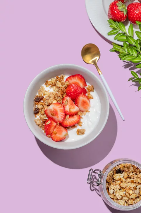 Granola or muesli with natural greek yogurt, strawberry in a bowl on a bright violet background with berries.